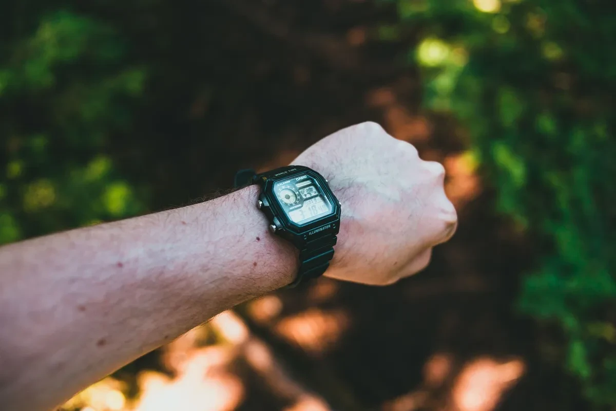 Casio AE-1200 negro con correa de resina en la muñeca, con árboles al fondo