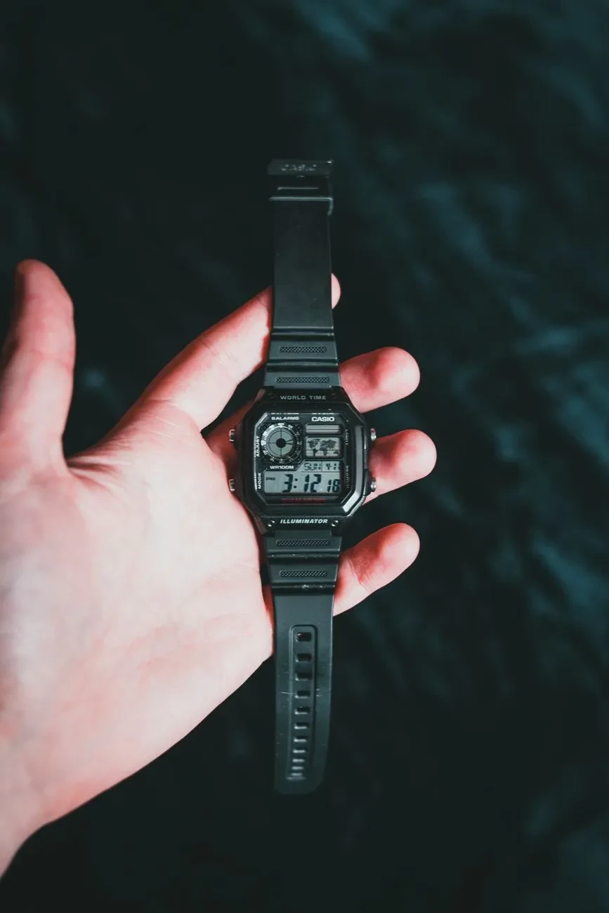 Mano sujetando un Casio AE-1200 negro con correa de resina sobre un fondo oscuro