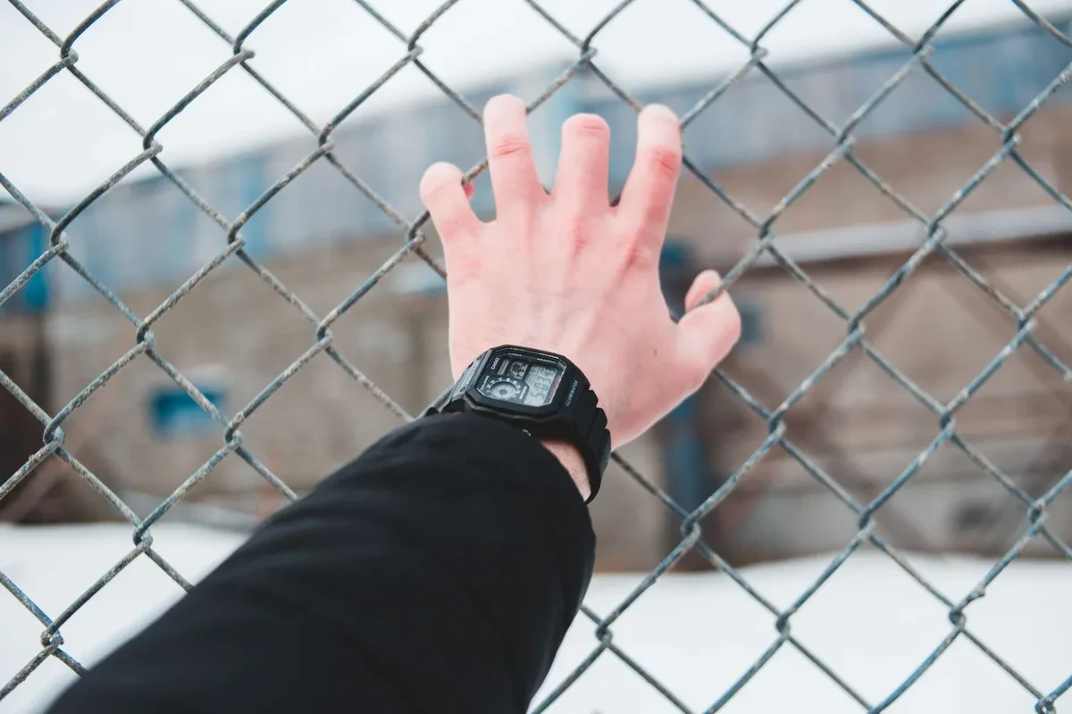 Mano con un Casio AE-1200 en la muñeca apoyada en una valla metálica