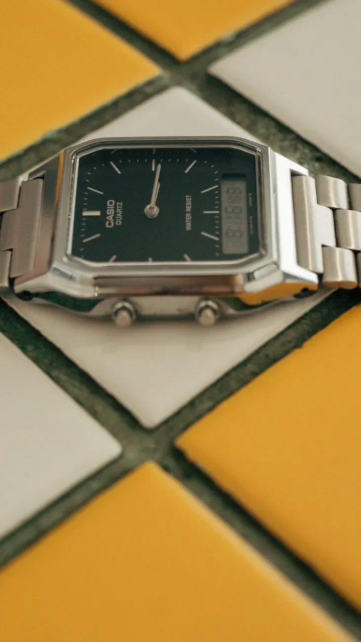 Casio AQ-230 plateado con esfera negra de agujas y pequeña pantalla digital, sobre baldosas amarillas y blancas
