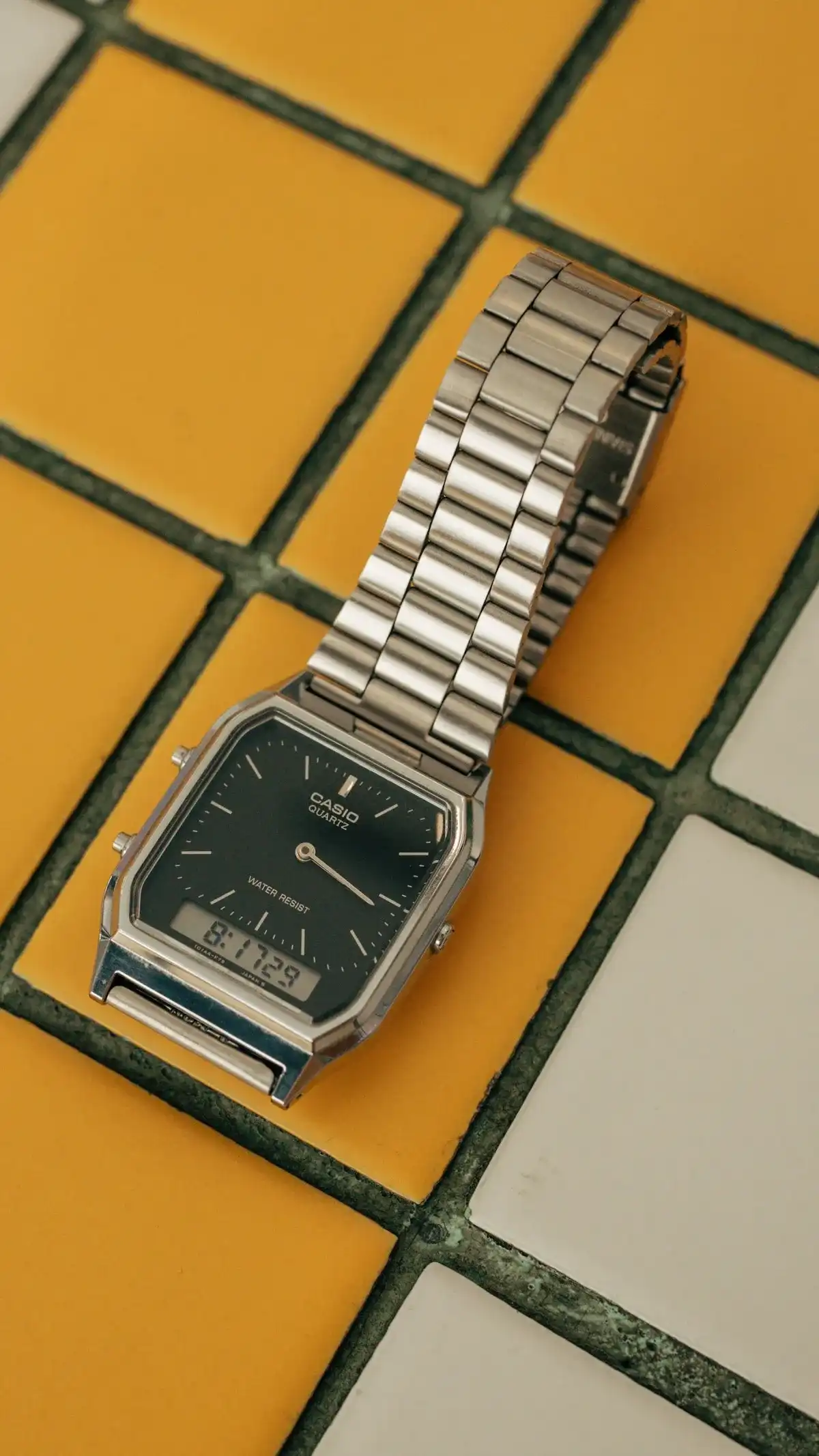 Reloj analógico-digital plateado con correa de acero sobre baldosas amarillas y blancas
