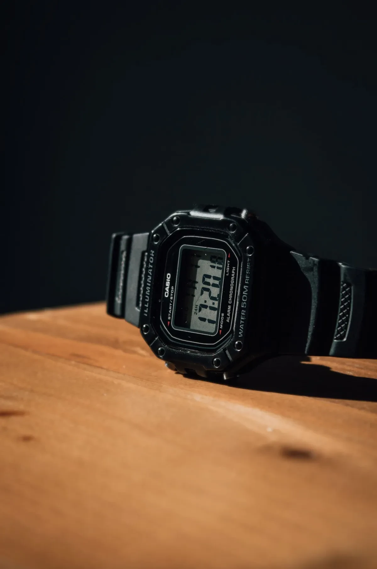 Casio digital negro de caja cuadrada sobre una mesa de madera, con la correa de resina