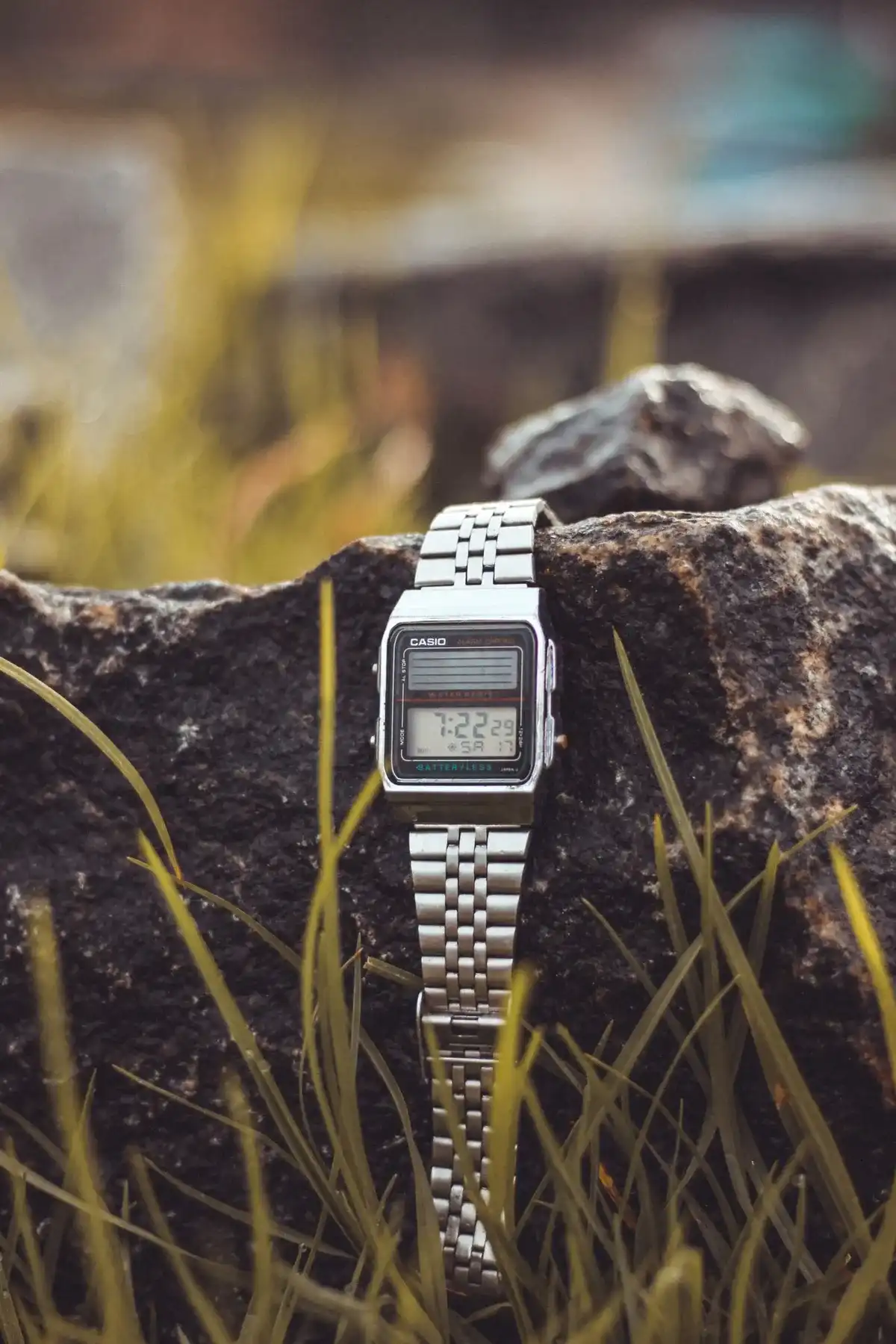 Casio Vintage digital plateado con correa de acero apoyado en una roca, con hierba alrededor