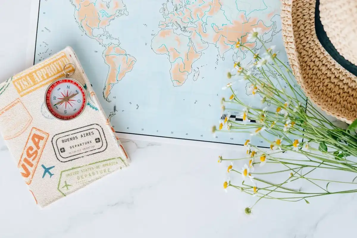 Mapa del mundo sobre una mesa con una brújula, un pasaporte y flores