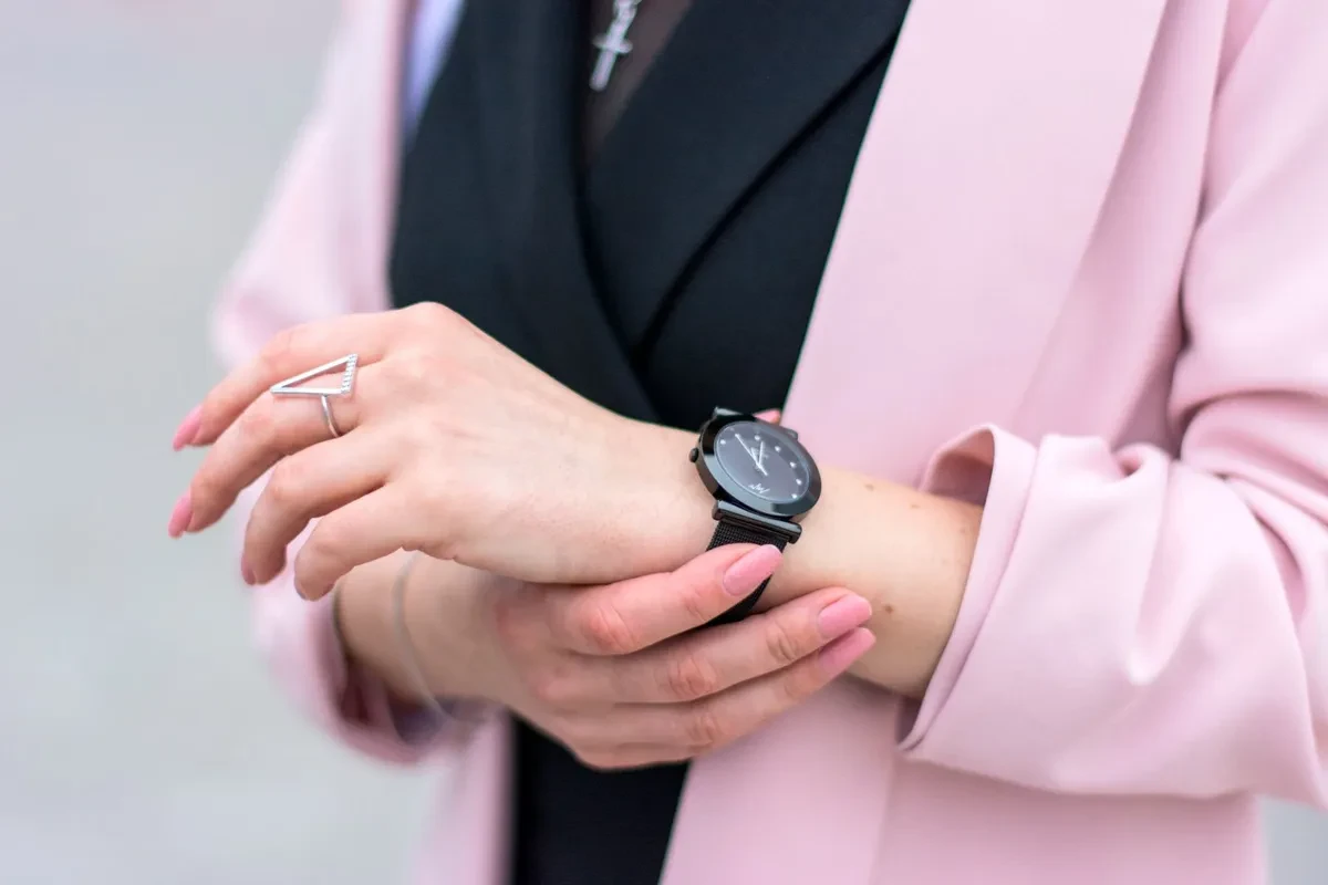 Mujer con un reloj analógico pequeño de correa fina en la muñeca, junto a una taza